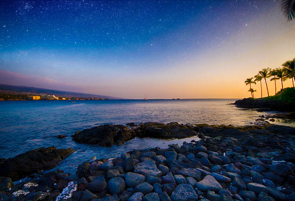 Rocky Kona coastline, palm trees and ocean at dusk